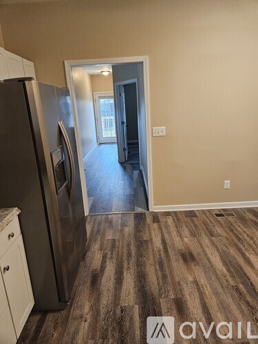 A kitchen with a refrigerator, cabinets, and a wooden floor leading to a hallway.