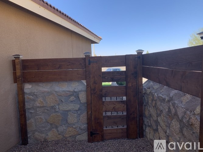 A wooden gate with a stone wall and a house in the background.