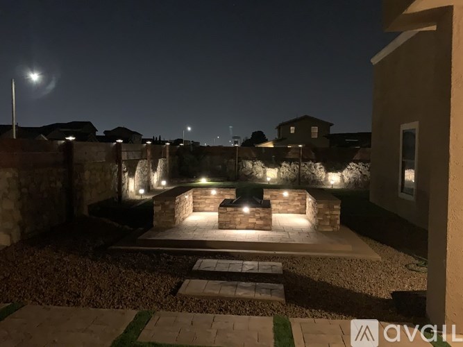A backyard at night with a lit fire pit and a moon in the sky.