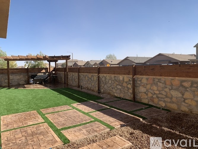 A backyard with a stone wall and a wooden pergola.