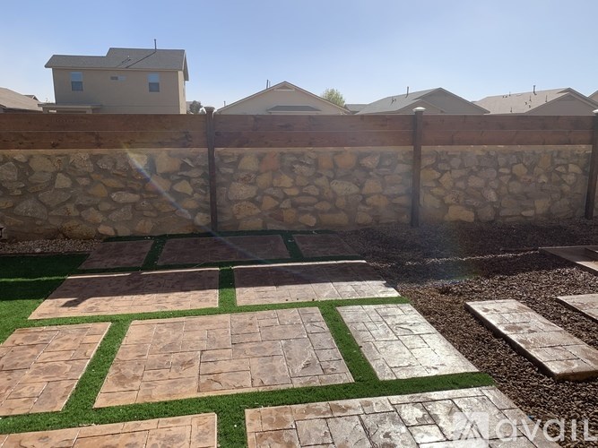 A backyard with a stone wall and a patterned concrete patio.