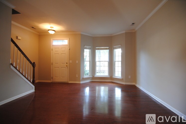 A spacious room with wooden floors and a staircase on the left side.