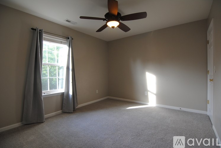 A room with a ceiling fan and a window with curtains.