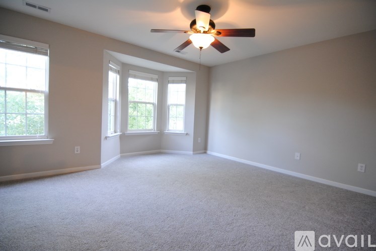 A room with a carpeted floor, a ceiling fan, and a window.
