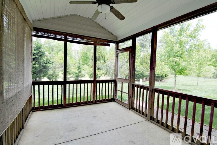 A screened porch with a ceiling fan and a view of a green lawn and trees.