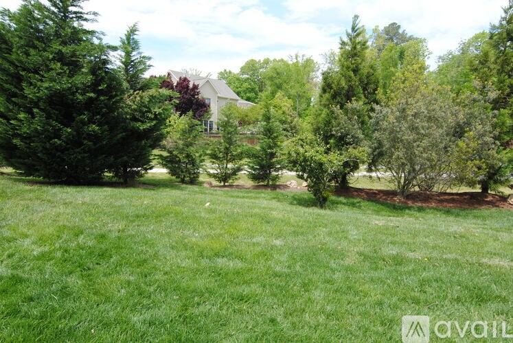 A grassy field with trees and a house in the background.