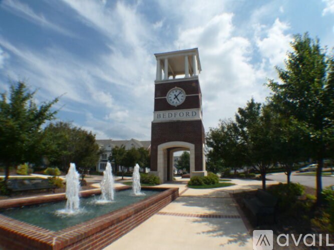 A clock tower in the middle of a park with a fountain in front of it.