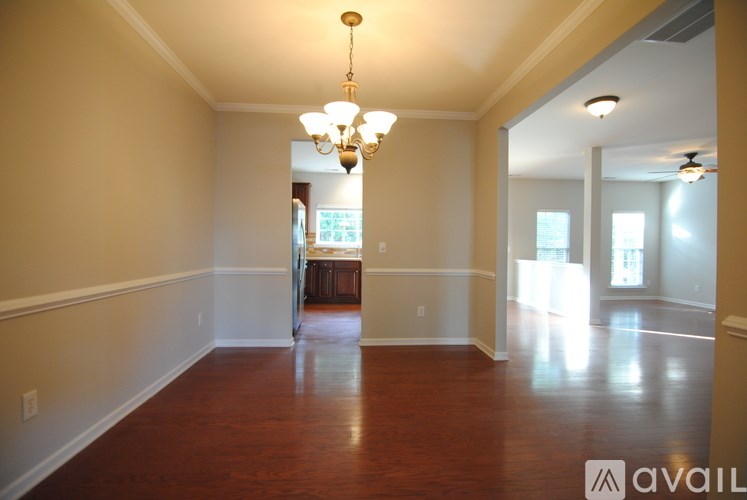 A large empty room with a chandelier and a view of a kitchen in the distance.