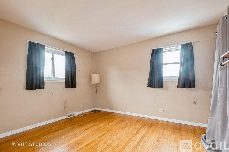 A room with wooden floors and two windows with blue curtains.