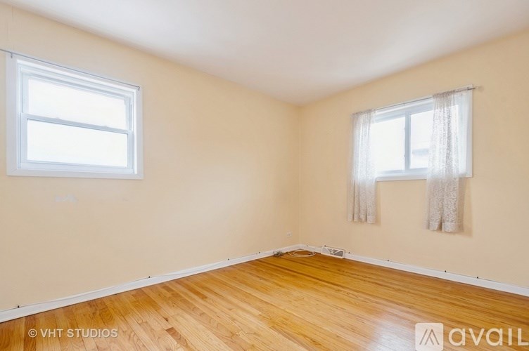 A room with wooden flooring and two windows.