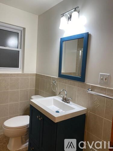 A bathroom with a toilet, sink, mirror and a window.