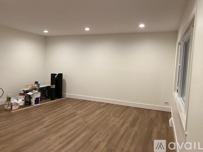 A room with wooden flooring and a white wall with a window.