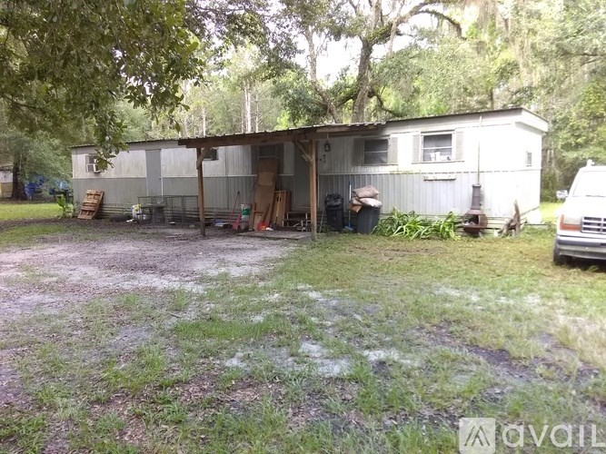 A white metal building with a garage door open is surrounded by trees and grass.