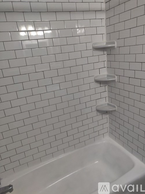 A white tiled bathroom with a white bathtub and a white shower head.