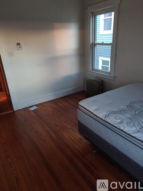 A bedroom with a bed, wooden floor, and a window.