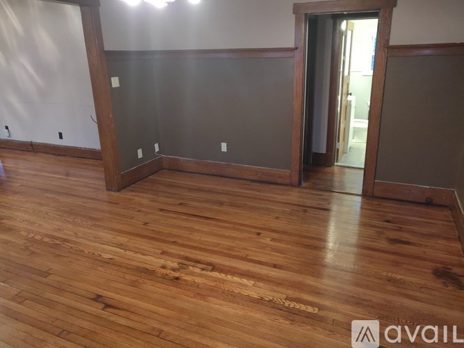 A room with wooden flooring and a doorway leading to another room.