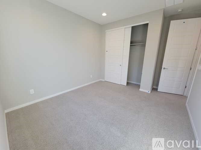 A spacious room with a carpeted floor and white walls, featuring a built-in fridge and a white door.
