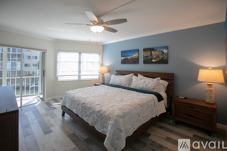 A bedroom with a large bed, a ceiling fan, and a view of a building outside the window.