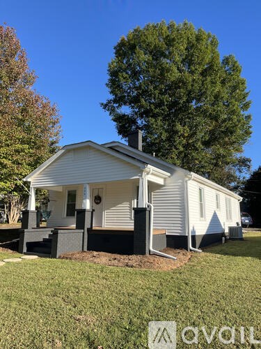 A white house with a porch and a tree in the background.