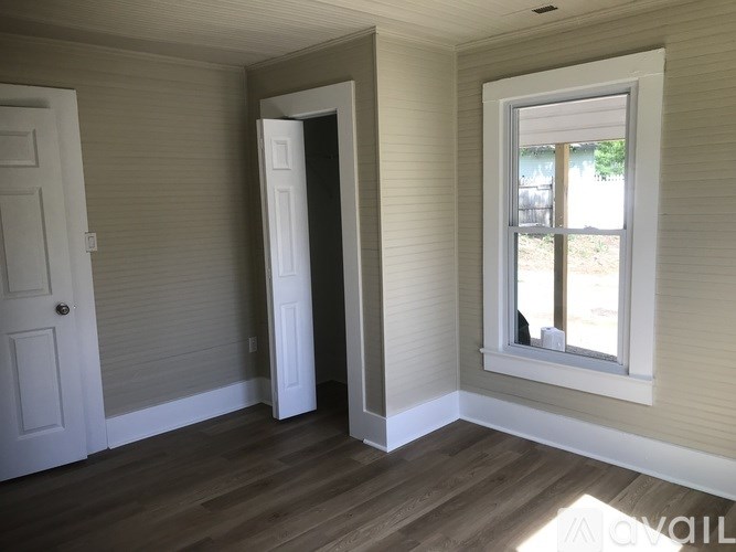 A room with a white door and a window with a view of a yard.