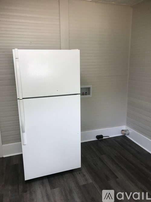 A white fridge in a room with wooden flooring.