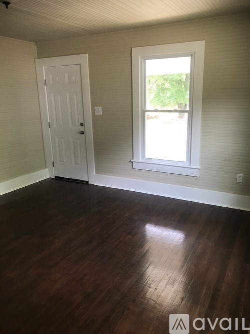 A room with a white door and a window with a view of a green tree.