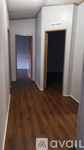 A hallway with a wooden floor and two doors, one of which is open.