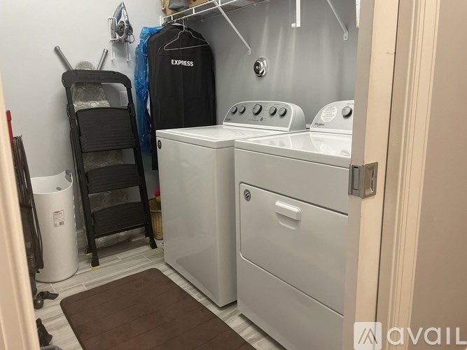 A laundry room with a washer and dryer, a chair, and a trash can.