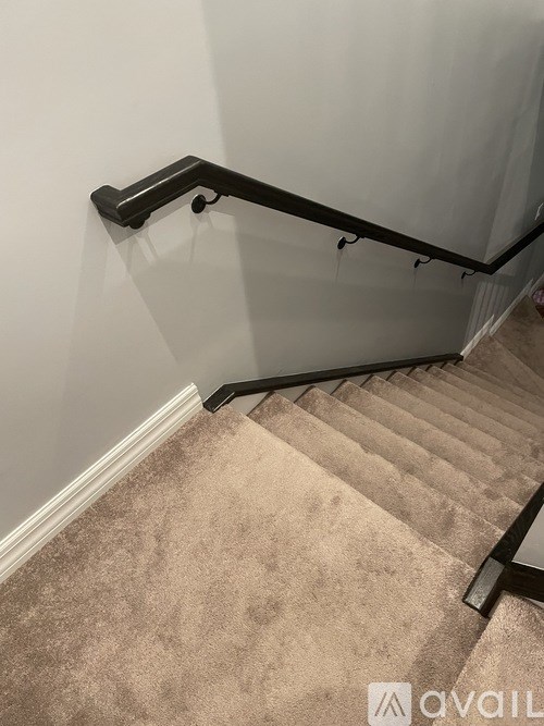 A staircase with a beige carpet and a black handrail.