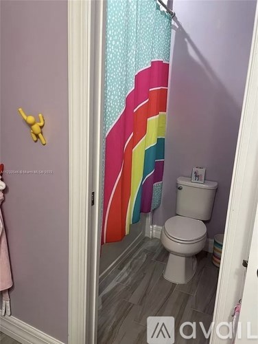 A bathroom with a toilet and a shower curtain with rainbow stripes.