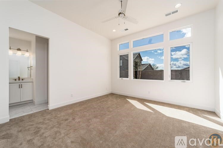 A room with a carpet floor, a ceiling fan, and a large window with a view of a house outside.