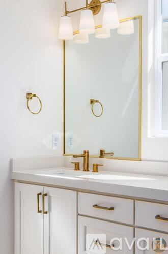 A bathroom vanity with a gold framed mirror and a gold light fixture.
