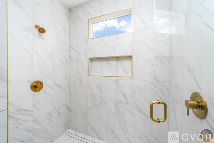 A white marble bathroom with gold fixtures and a small window.