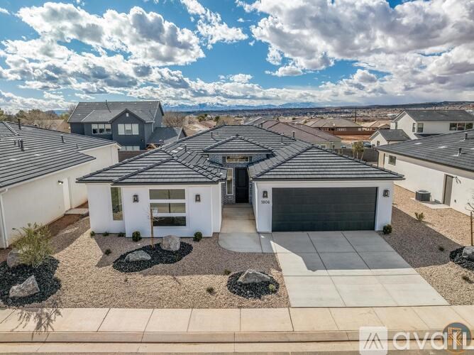 A white house with a black roof is surrounded by other similar houses.