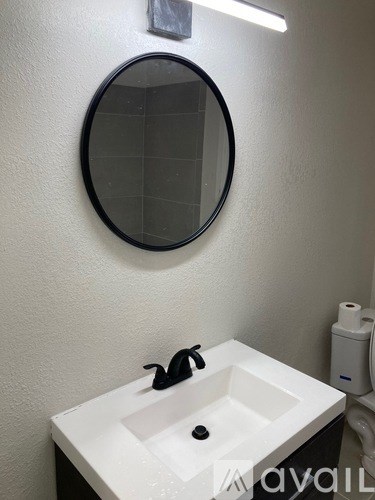 A white sink with a black faucet under a round mirror.