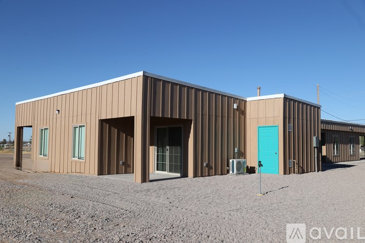 A large brown building with a blue door stands in a gravel lot.