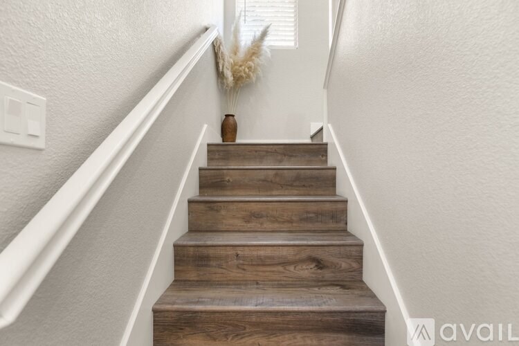A wooden staircase with a white railing and a vase on the top step.