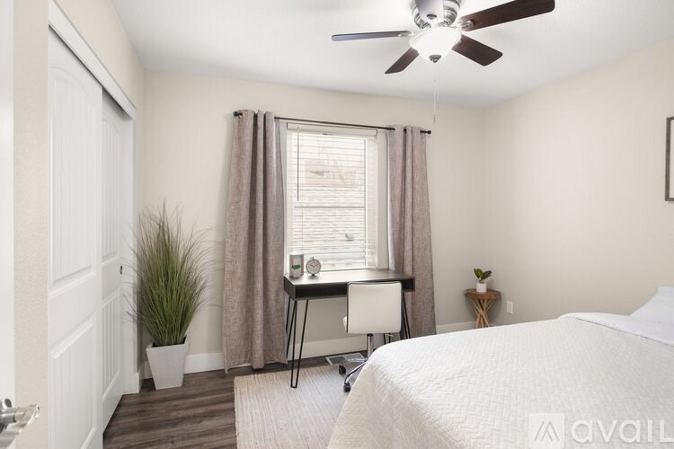 A bedroom with a bed, desk, chair, and a ceiling fan.