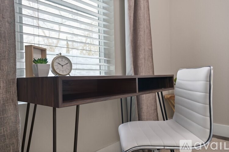 A white chair sits in front of a wooden desk with a clock and plant on it.