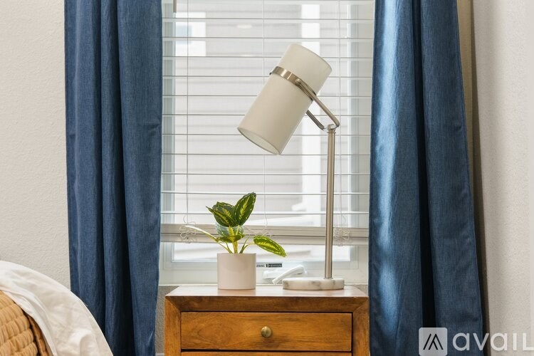 A lamp with a white shade is on a wooden table next to a plant.
