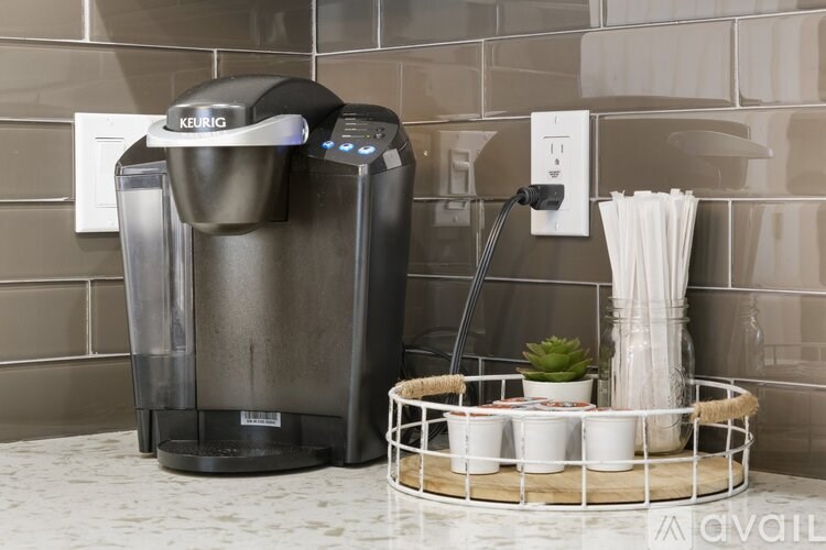 A Keurig coffee maker is on a countertop with a tray of cups and a plant.