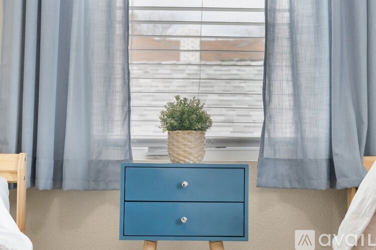 A blue drawer with a plant on top sits in front of a window with grey curtains.