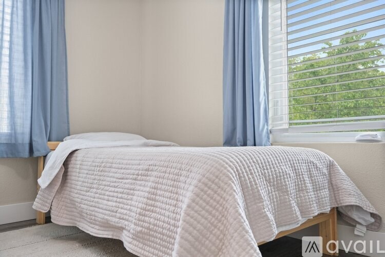 A bed with a checkered blanket is in a room with a window.