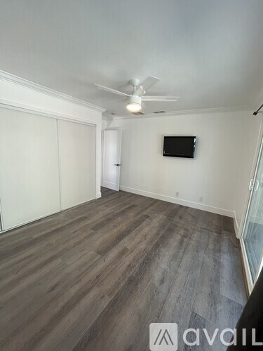A room with a ceiling fan and a flat screen TV mounted on the wall.