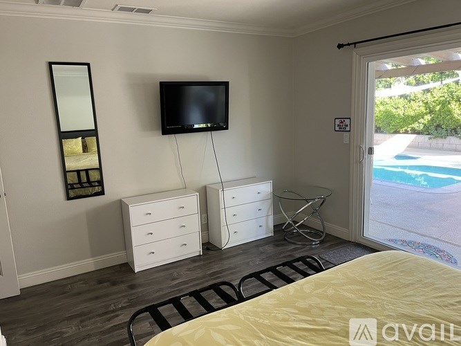 A bedroom with a bed, dressers, and a television.