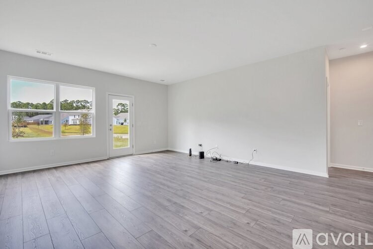 A spacious room with wooden flooring and large windows overlooking a green landscape.