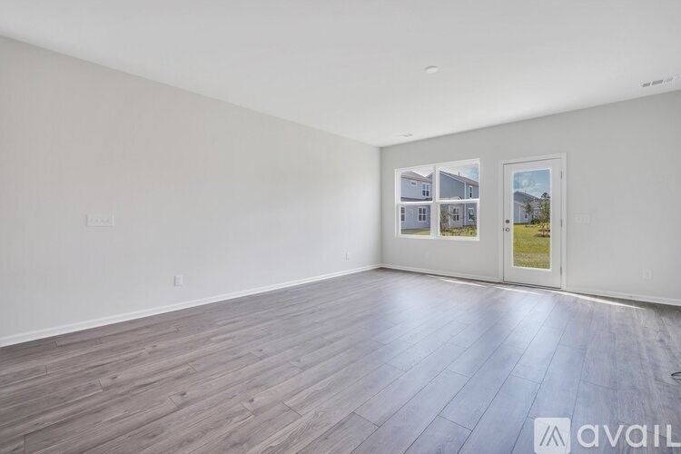 A spacious room with wooden flooring and two windows showing a view of a house and a lawn.