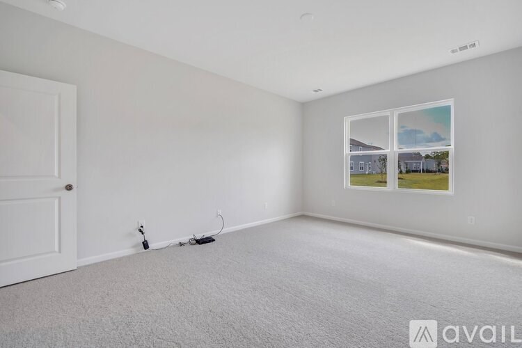 A room with a white door and a carpeted floor with a picture frame on the wall.