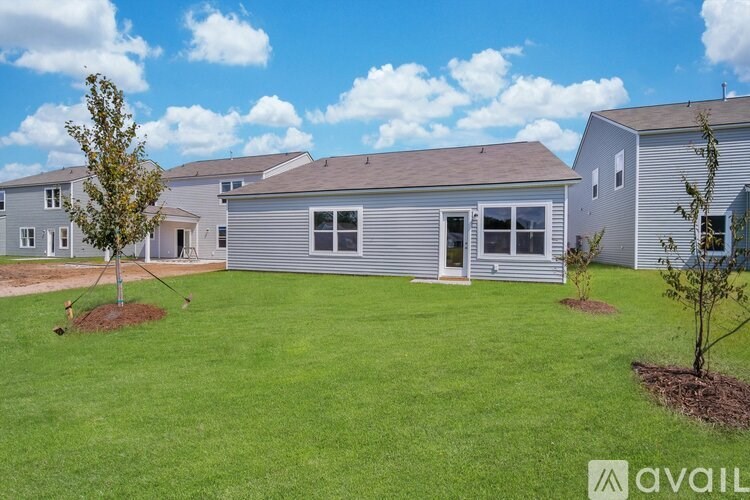 A house with a grey siding and a brown roof is surrounded by a green lawn.
