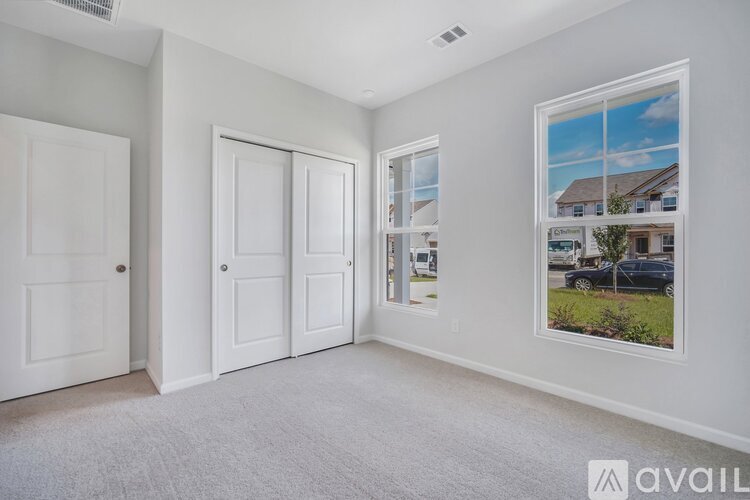 A room with white walls and carpeted floor with a picture of a house on the wall.